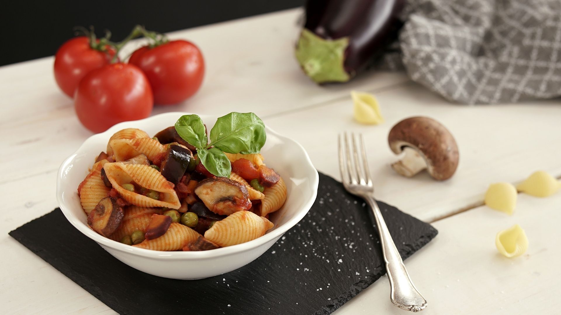 Muschelnudeln mit Gemüseragù in einer weißen Schüssel auf einer schwarzen Schieferplatte.