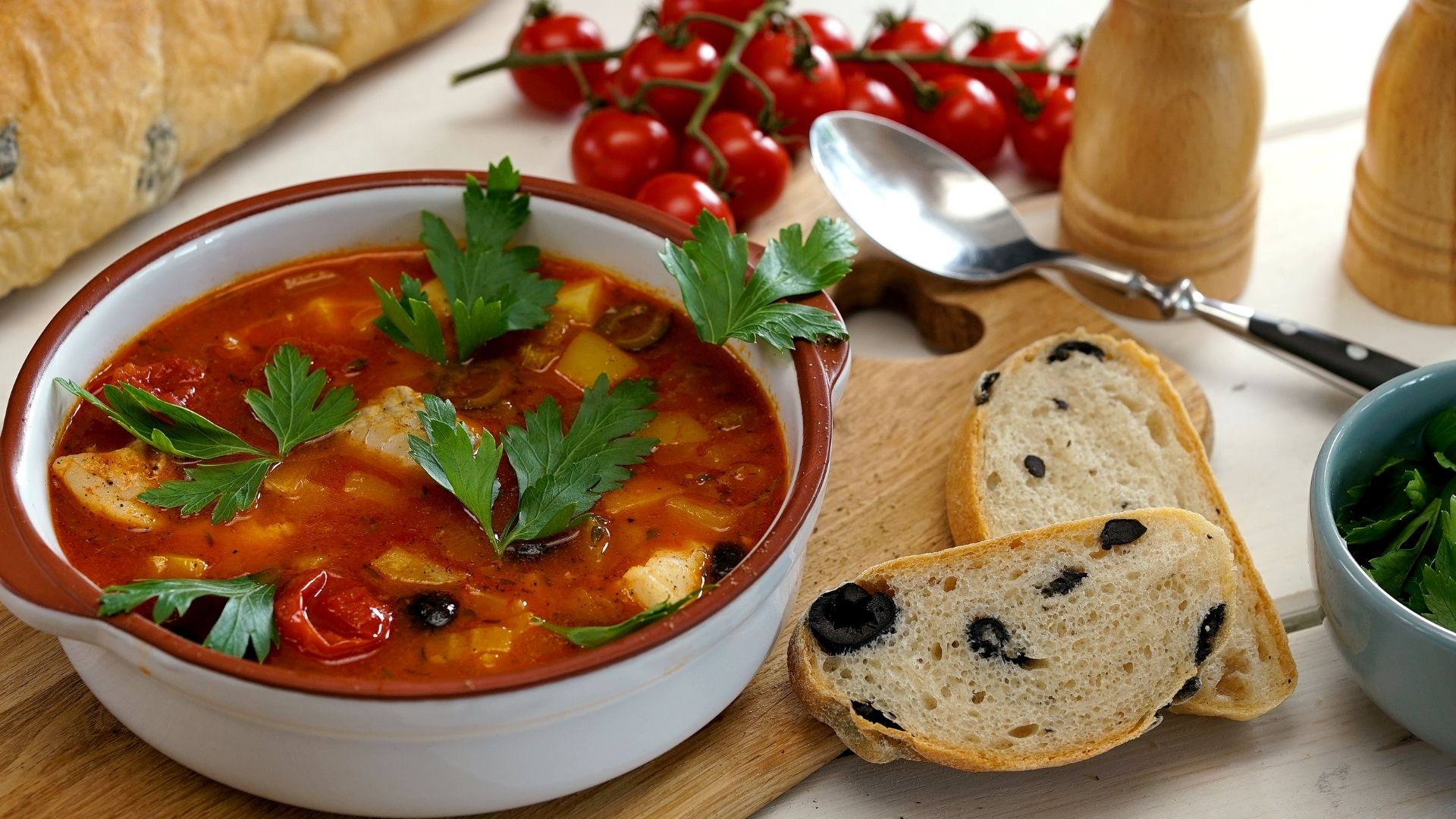 Eine Schüssel mit Tomaten-Fischsuppe, daneben zwei Scheiben Olivenbrot