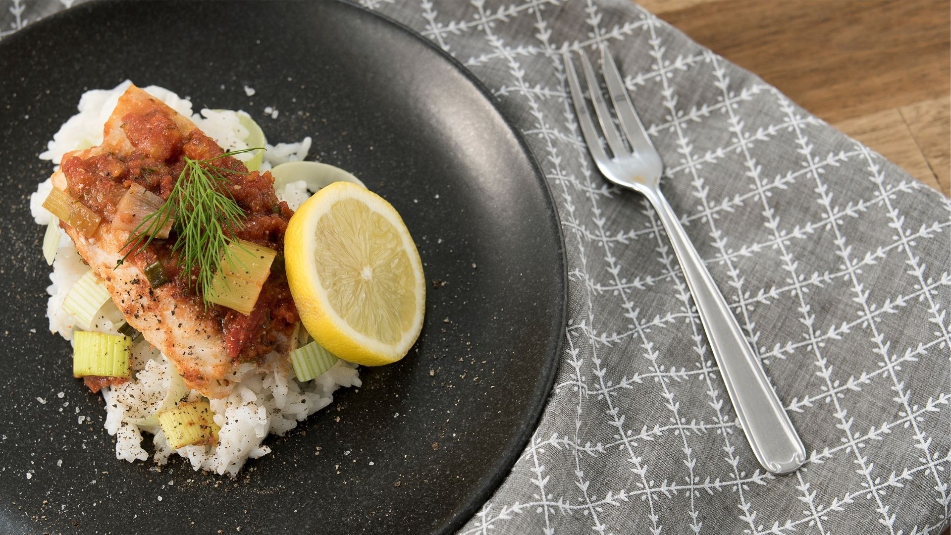 Ein Teller mit Reis, Rotbarschfilet und einer Scheibe Zitrone